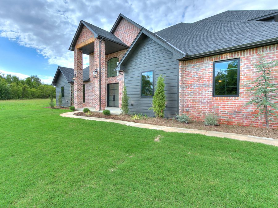 Side view of the front lawn of the brick home with a dark colored roof as well as dark panel accent walls.