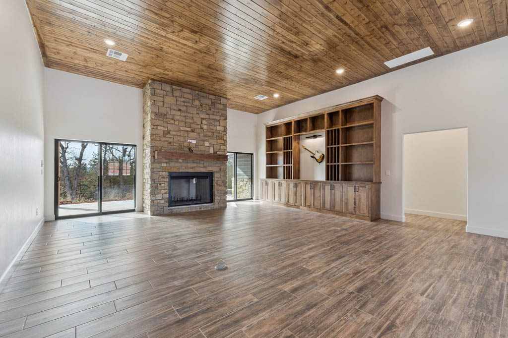 A living room featuring wood floors and celing, with a stone fireplace and built in shelving on the wall. There are two sliding doors on either side of the fireplace, leading to an outdoor patio.