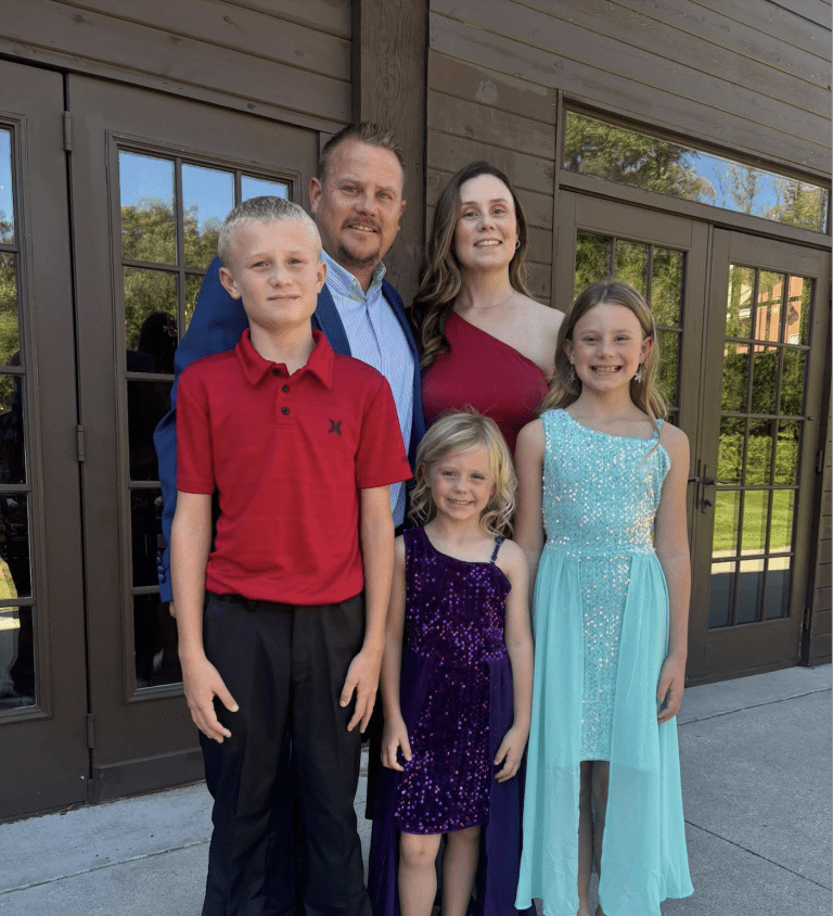 Photo of the Julian family (husband, wife, and three children) nicely-dressed, and standing outside together.